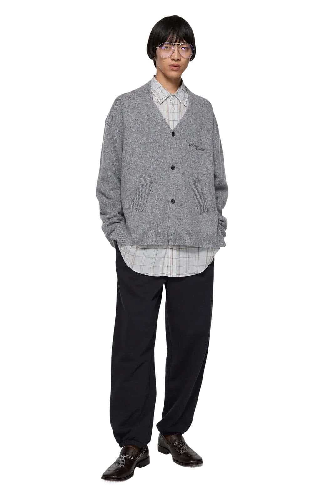 Model in a grey cardigan and dark trousers against a white backdrop